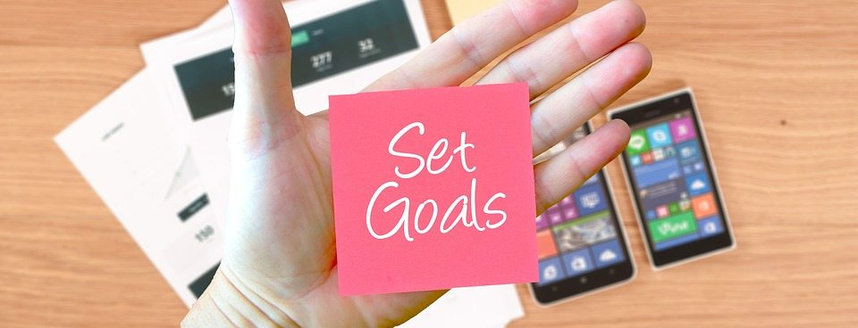 image of person holding a sticky note with set goals on it for article An Entrepreneur's Guide to Google Analytics [Infographic]